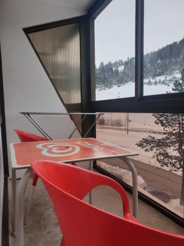 une table et deux chaises rouges devant une fenêtre dans l'établissement Résidence belle hutte coté pistes de ski, à La Bresse