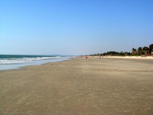 a beach with people walking on the sand and the ocean at Palm Grove Cottages - Leisure Resort in Benaulim
