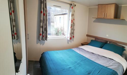 ein Schlafzimmer mit einem blauen Bett und einem Fenster in der Unterkunft Mobil-Home Cosy - Matelas qualité hôtel in Passy