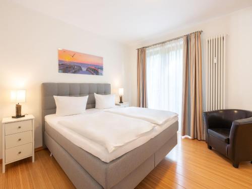 um quarto com uma grande cama branca e uma cadeira em Kaiservillen Heringsdorf - Ferienwohnung mit 1 Schlafzimmer und Balkon D214 em Heringsdorf