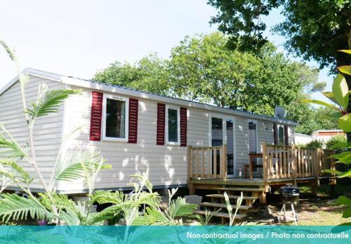 a white tiny house with red shutters and a deck at Camping Officiel Siblu Domaine de Litteau in Litteau