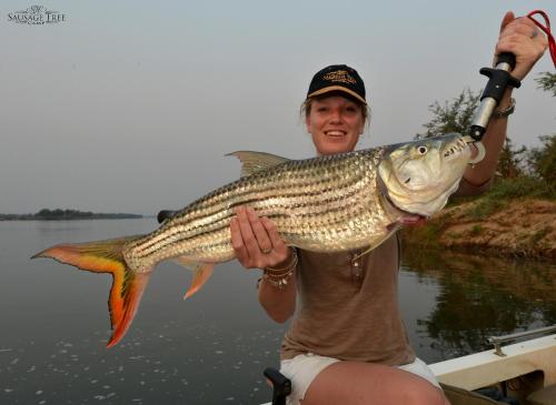 a woman holding a large fish in a boat at Sausage Tree Camp in Jeki