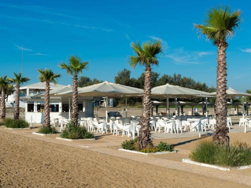 a row of palm trees and white tables and chairs at Apartment in Albarella near Sandy Beach in Isola Albarella