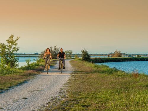 two people riding bikes down a dirt road next to a river at Apartment in Albarella near Sandy Beach in Isola Albarella