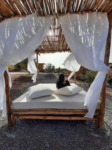 a woman sitting on a bed under a thatch roof at Le Parc des Oliviers in Marrakech