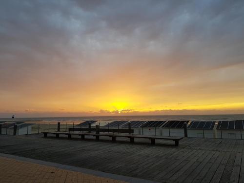 a bench on a pier with the sunset in the background at You, me and the sea - seaview groundfloor appartment in Ostend