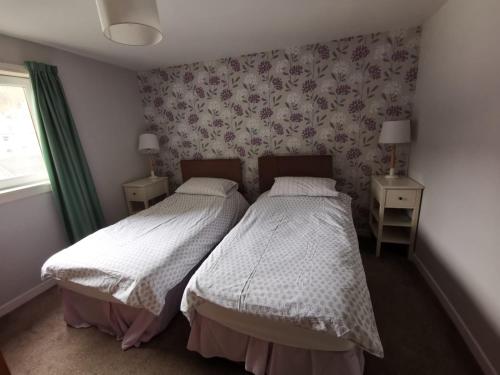 two beds in a bedroom with floral wallpaper at Kings Arms Holiday Apartments in Oban