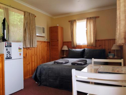 1 dormitorio con 1 cama, mesa y nevera en Twelve Apostles Motel & Country Retreat en Princetown