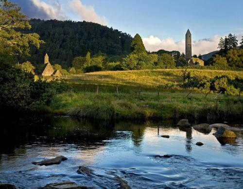 a river in a field with a building in the background at Glendalough International Youth Hostel in Laragh