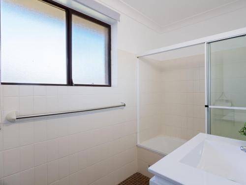 a white bathroom with a sink and a window at Promenade, 12 8 Intrepid Cl - fantastic waterfront unit with air con and WiFi in Nelson Bay