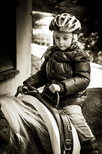a young child wearing a helmet riding a horse at Landhotel Spreitzhofer in Sankt Kathrein am Offenegg