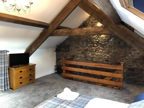 a bedroom with a bed and a tv and a stone wall at The Grooms Cottage in Llanrug