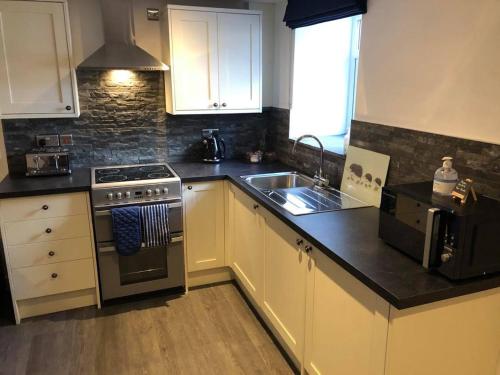 a kitchen with white cabinets and a stove and a sink at The Grooms Cottage in Llanrug