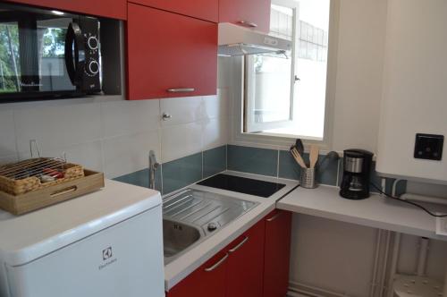 Elle comprend une petite cuisine avec des placards rouges et un évier. dans l'établissement Appartement Pour 2 Personnes Vue Sur Le Port- Residence Jean Rameau, à Hossegor