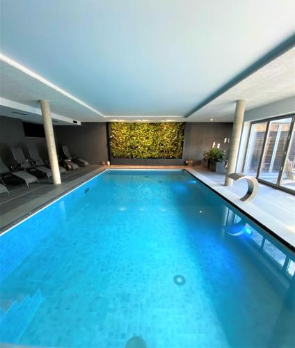 a large swimming pool with blue water in a building at Hôtel WELLNESS EAU DE ROCHE Durbuy in Durbuy