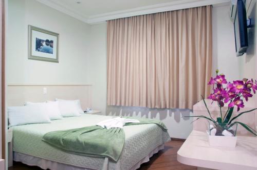 a bedroom with a bed and a vase of flowers at Grande Hotel Guarapuava in Guarapuava