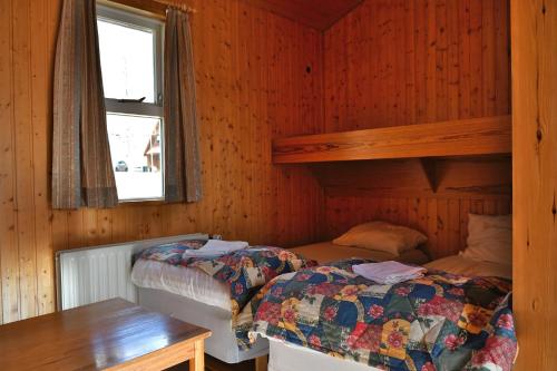 two beds in a wooden room with a window at Kaffi Holar Cottages and Apartments in Sauðárkrókur
