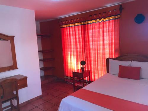 a bedroom with a bed and a window with red curtains at Hotel La Cascada in Oaxaca City