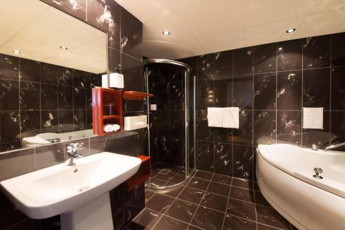 a black tiled bathroom with a sink and a tub at Clarion Collection Hotel Grimstad in Grimstad
