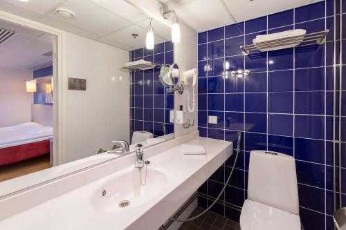 a blue tiled bathroom with a sink and a toilet at Scandic Hakaniemi in Helsinki