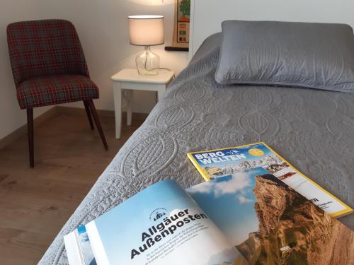 a bed with two magazines on it with a chair at Apartment Gästehaus Maria in Rettenbach am Auerberg