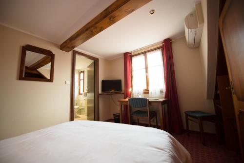 a bedroom with a bed and a desk and a window at Logis Hotel Restaurant A L'Etoile in Mittelhausen