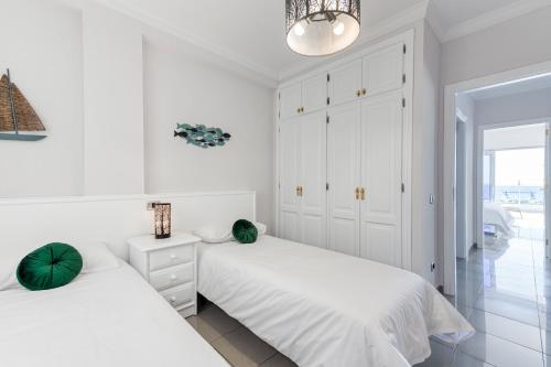 a white bedroom with two beds and a chandelier at BeachFront in Puerto Mogán in Puerto de Mogán