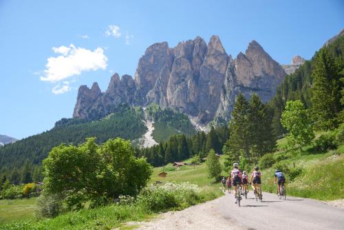a group of people riding bikes down a road in the mountains at Hotel Soreghes Gran Chalet in Campitello di Fassa