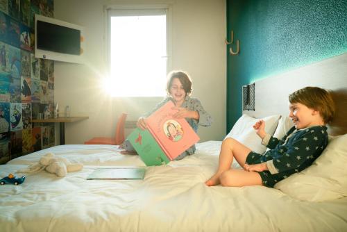 two children sitting on a bed with a book at hotelF1 Chambéry Nord Rénové in Chambéry
