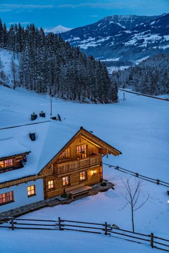 a log cabin in the snow with the lights on at Almchalet Linharterhof in Haus im Ennstal