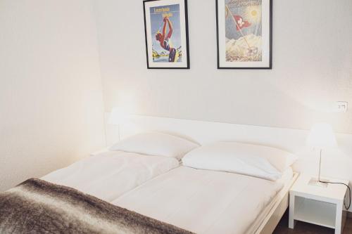 a white bed with two framed posters on the wall at Kurhaus Lenzerheide in Lenzerheide