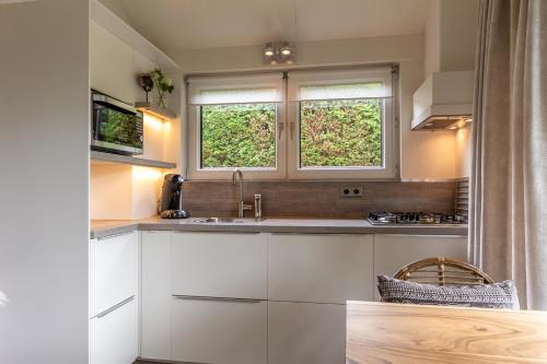 cocina con armarios blancos y 2 ventanas en Vakantiewoning met privé sauna, en Schoorl