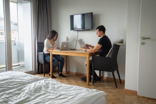 a man and woman sitting at a table with a laptop at Nyon Hostel in Nyon