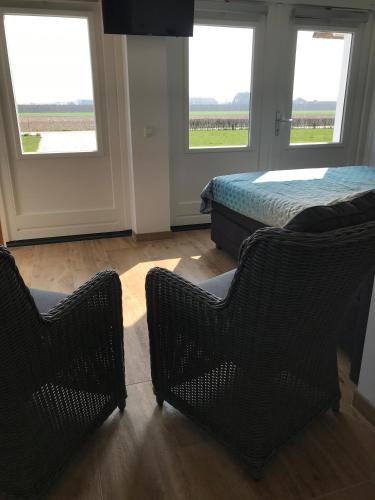 a bedroom with two chairs and a bed and windows at B&B De Spiegel - Genieten van rust en ruimte in Cothen