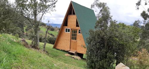 una pequeña casa con techo verde en una colina en ANIMALS GALMPING, en Guasca