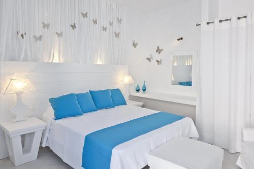 a white bedroom with a white bed and blue pillows at Casa Florina in Imerovigli