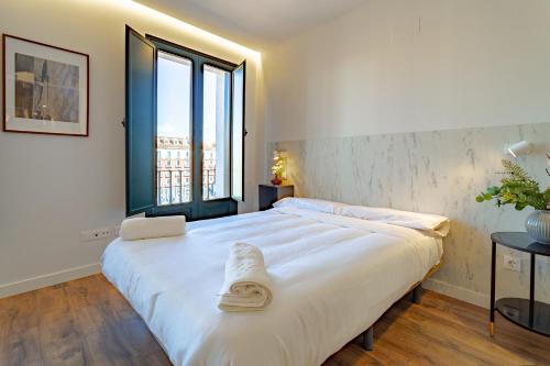 a bedroom with a large white bed with a large window at Edificio 13 by Plaza Mayor Apartamentos in Valladolid