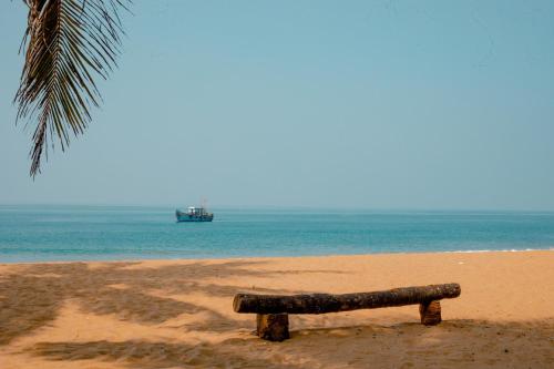 a bench on the beach with a boat in the water at Malabar Ocean Front Resort And Spa, Bekal in Nīleshwar