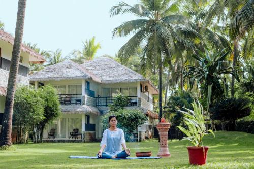 a woman sitting in a yoga pose in front of a house at Malabar Ocean Front Resort And Spa, Bekal in Nīleshwar