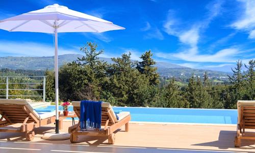 eine Terrasse mit 2 Stühlen, einem Sonnenschirm und einem Pool in der Unterkunft Orientem Villa Heated Pool in Georgioupoli