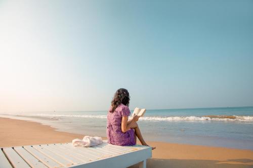 a woman sitting on a bench reading a book on the beach at Malabar Ocean Front Resort And Spa, Bekal in Nīleshwar