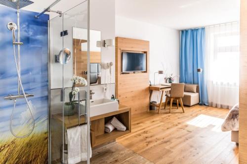 a bathroom with a shower and a television in a room at Das Aunhamer Suite & Spa Hotel in Bad Griesbach