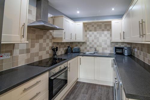 a kitchen with white cabinets and black counter tops at Old Station Cottages in Aberfeldy