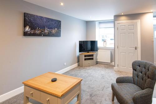 a living room with a tv and a chair and a table at Old Station Cottages in Aberfeldy