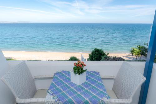 a table with a vase of flowers on a balcony with the beach at Theoxenia Chios Apartments in Paralia Agias Foteinis