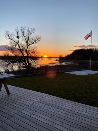 a sunset over the water with a bench and a flag at Houses with a View#Sauna#Jaccuzi in Gozdowice