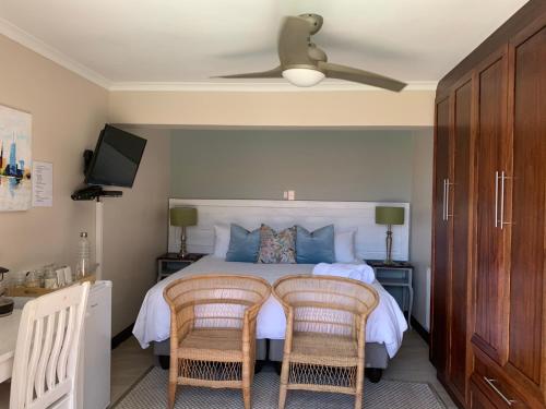 a bedroom with a bed with two chairs and a ceiling fan at Bokamoso Views in Rustenburg
