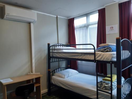 a room with two bunk beds and a desk and a window at Ariki Backpackers in New Plymouth