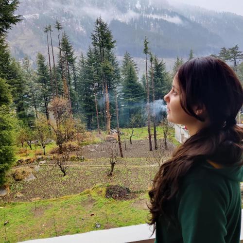 a woman looking out of a window at a forest at Safar Hostel Manali in Manāli