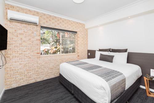 a bedroom with a large bed and a brick wall at Coopers Colonial Motel in Brisbane